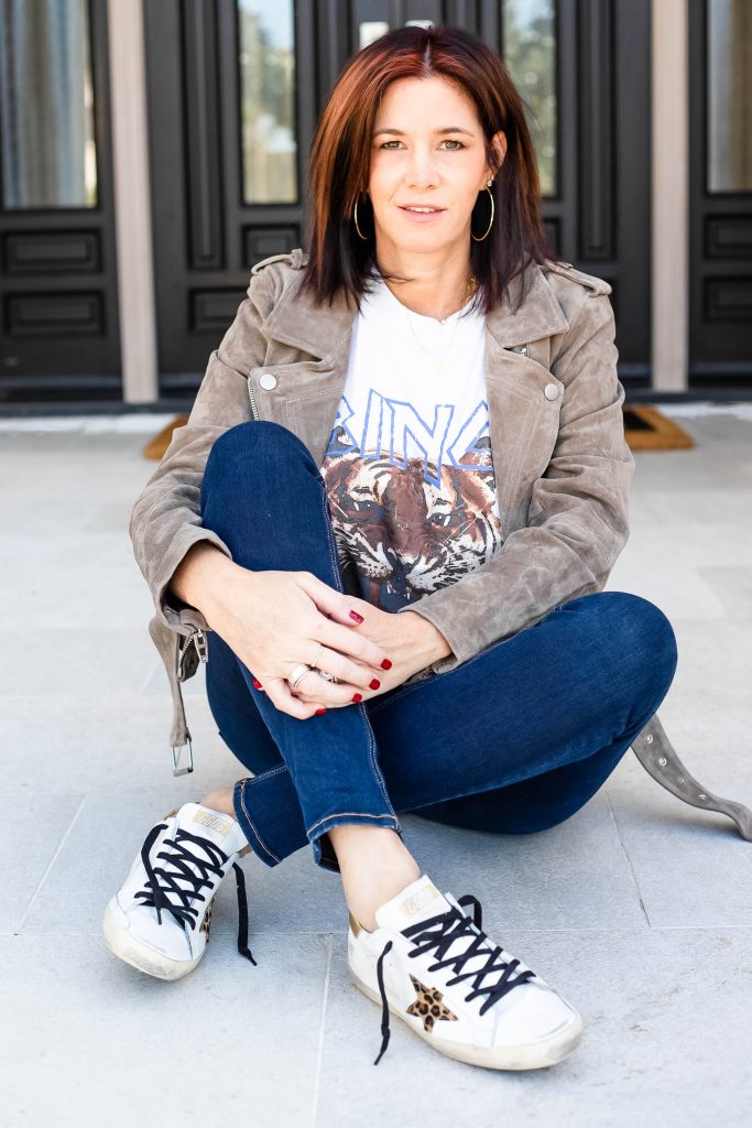 Midlife women seated wearing Golden Goose Sneakers, jeans, Anine Bing Tee and Suede Jacket