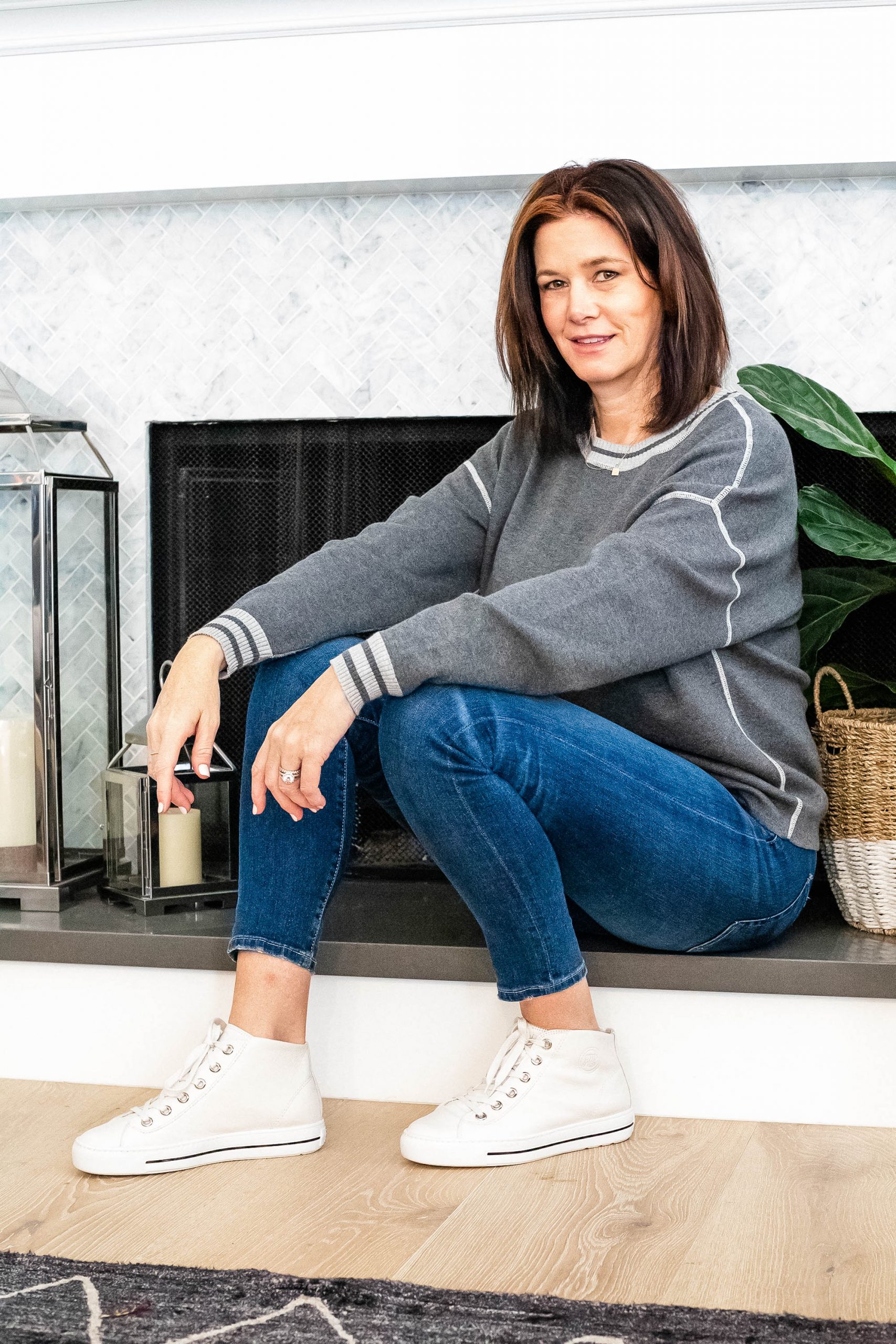 Midlife women sitting wearing white sneakers, jeans and grey sweater