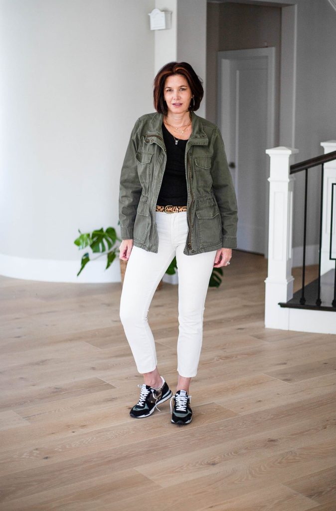 Midlife women wearing ivory jeans with black top and utility jacket and golden goose sneakers.