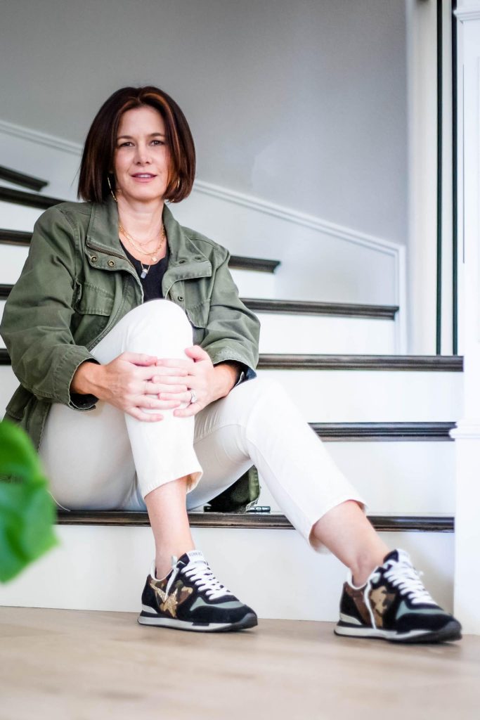 Midlife women wearing ivory jeans with black top and utility jacket and golden goose sneakers.