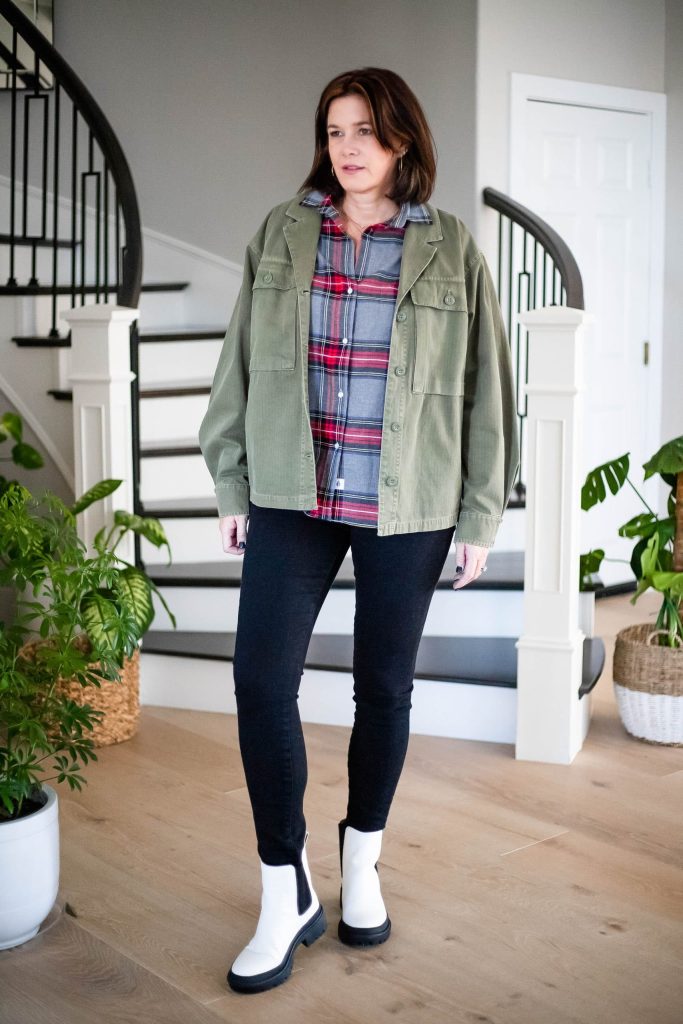 Over 50 women wearing flannel shirt, black jeans, Utility Jacket and white lug sole boots.