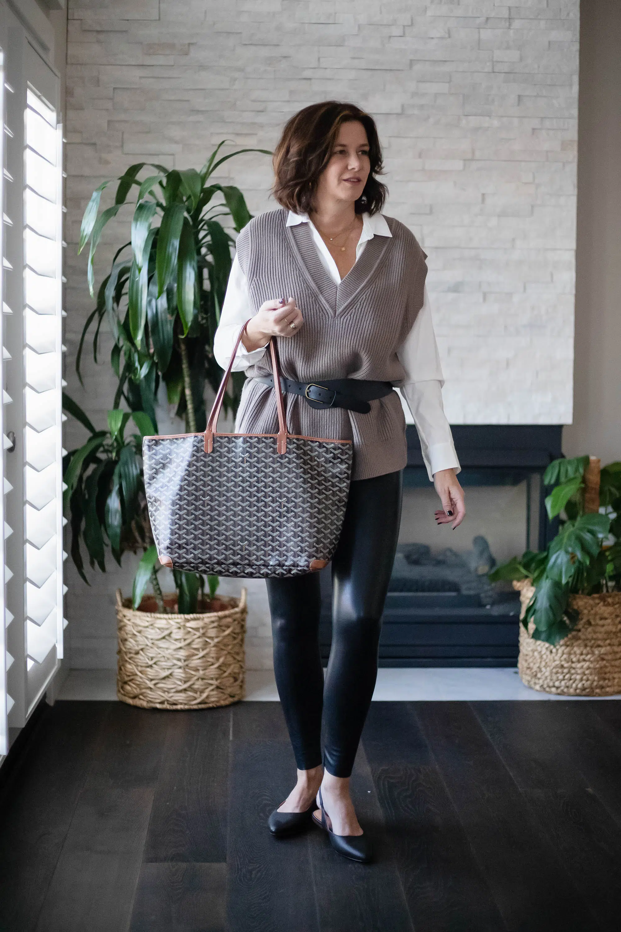 Women wearing Zara sweater vest, Commando faux leather leggings, white shirt and carrying Goyard purse