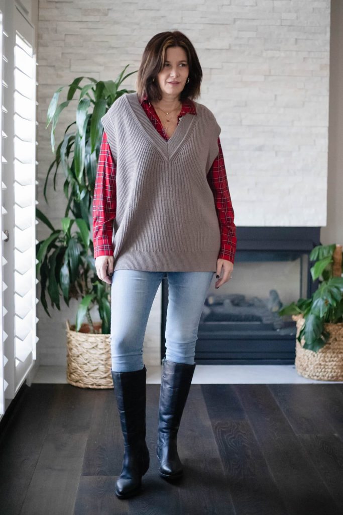 Women wearing Zara sweater vest, plaid shirt, jeans and tall boots.