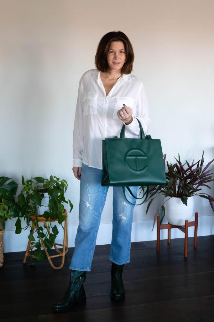 Women wearing white blouse, ripped jeans, Aquatalia green boots and carrying Teslar bag.