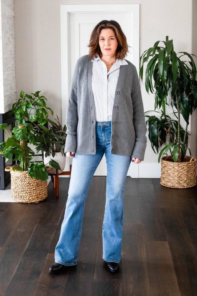 Over 50 women wearing bootcut jeans, button up shirt and grey cardigan.