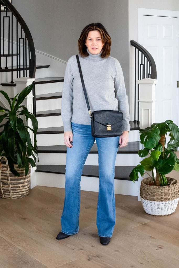 Over 50 women wearing bootcut jeans, grey cashmere turtleneck, booties and Louis Vuitton purse.