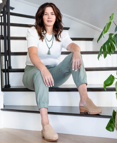 Midlife women wearing clogs, pale green pants, cream puff sleeve shirt and necklace