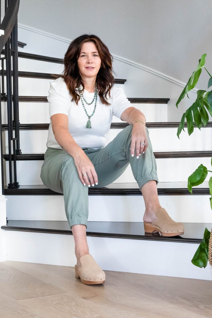 Midlife women wearing clogs, pale green pants, cream puff sleeve shirt and necklace