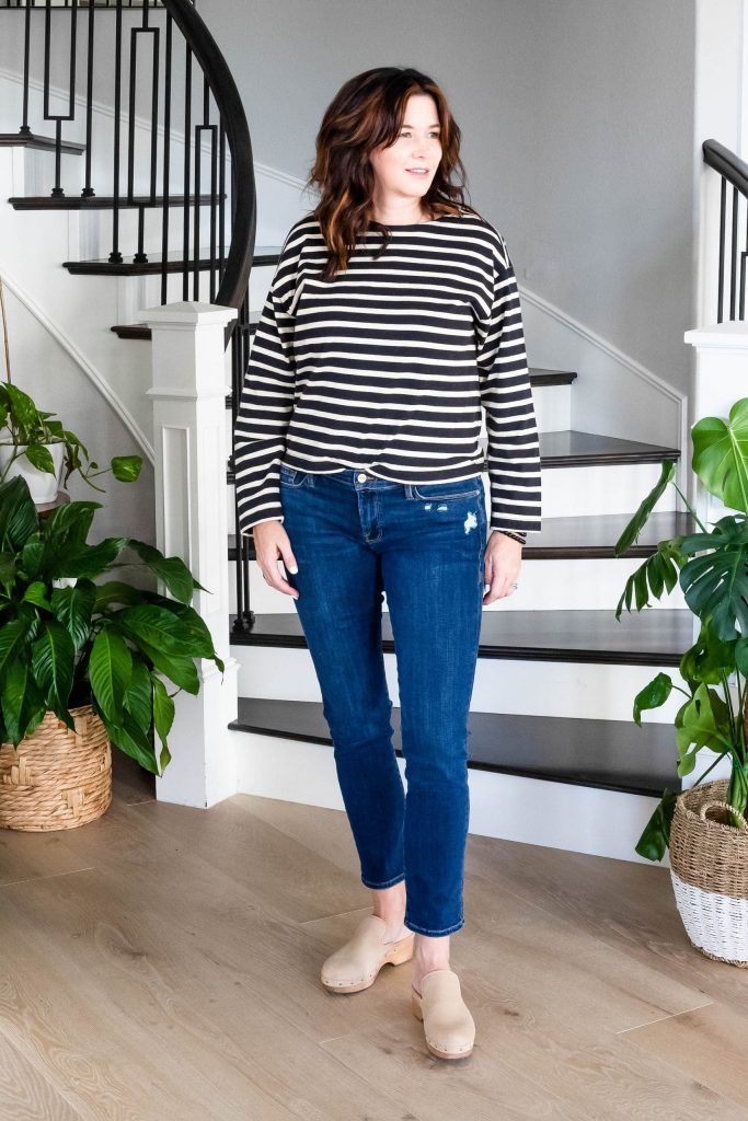 Midlife women wearing clogs, dark wash jeans and striped shirt.