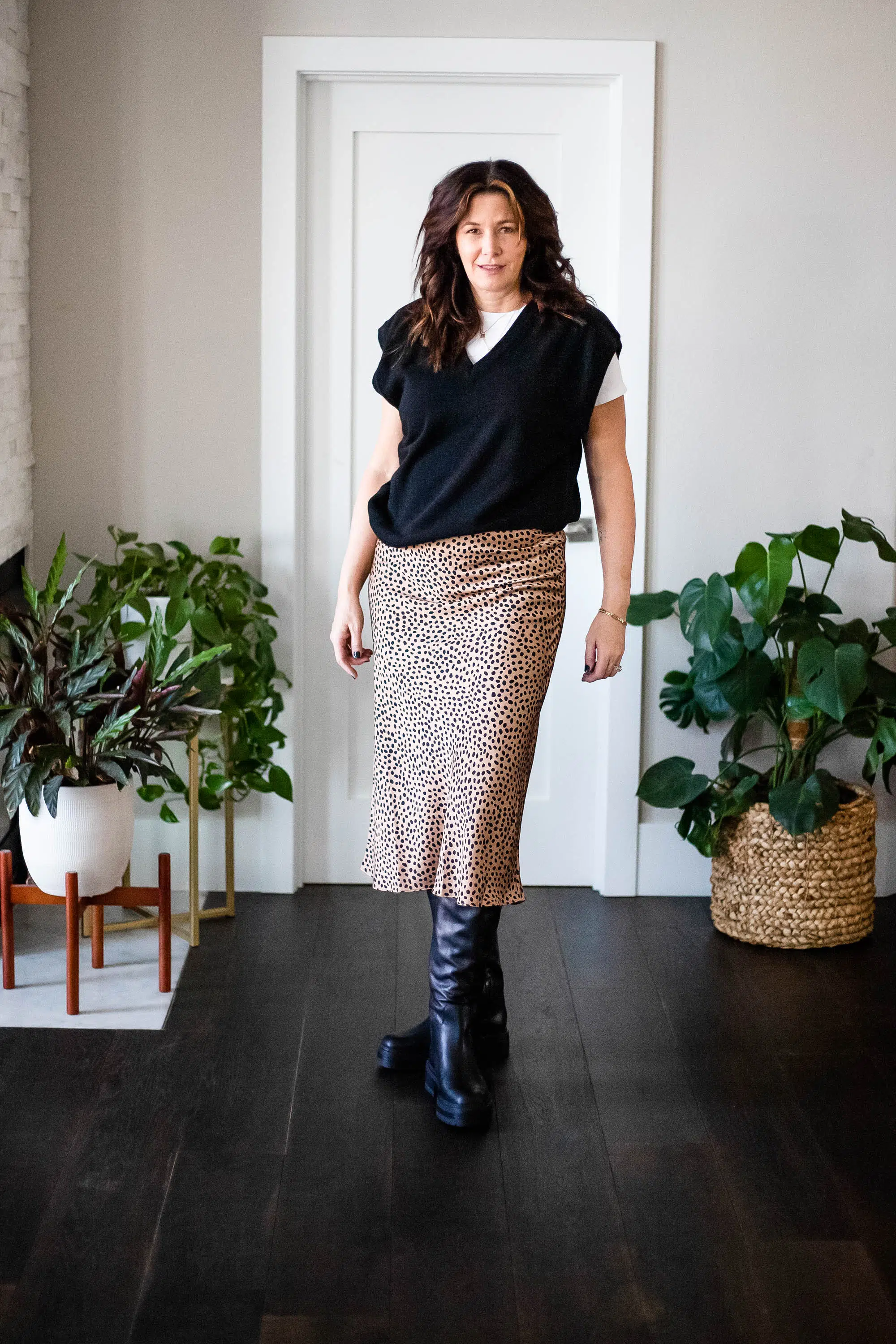 Midlife women wearing sweater vest, white tshirt, satin skirt and boots.