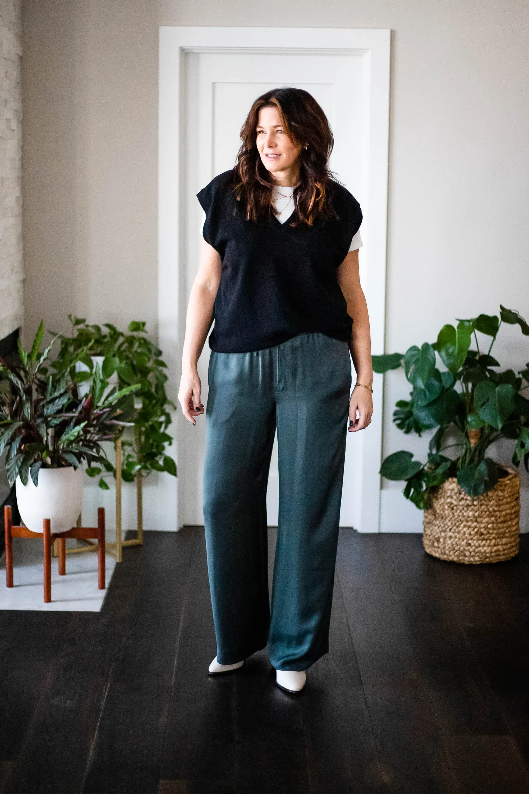 Midlife women wearing sweater vest, white tee, satin pants & booties