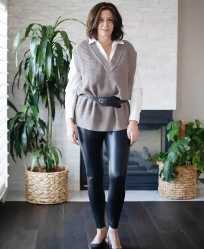 Midlife women wearing sweater vest, button down shirt, faux leather leggings and heels.